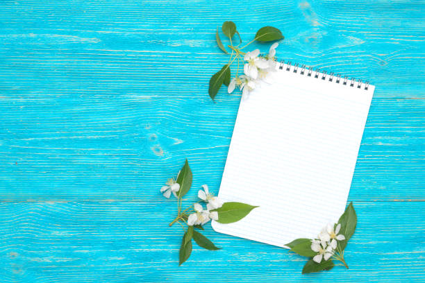 open blank notepad with white blooming on turquoise wooden background