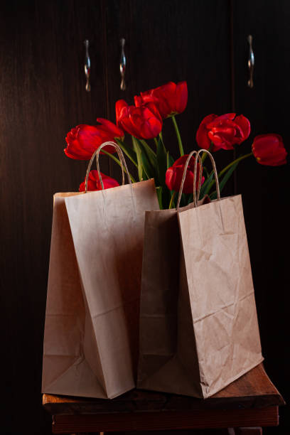 Kraft paper bags with blooming red tulips bouquet on black background.Donations help recycling boxes, dark moody low key Kraft paper bags with blooming red tulips bouquet on black background. Dark moody low key minimalism style flowers and food delivery packaging banner copy space mockup. Donations help recycling boxes. Slective Focus stock pictures, royalty-free photos & images