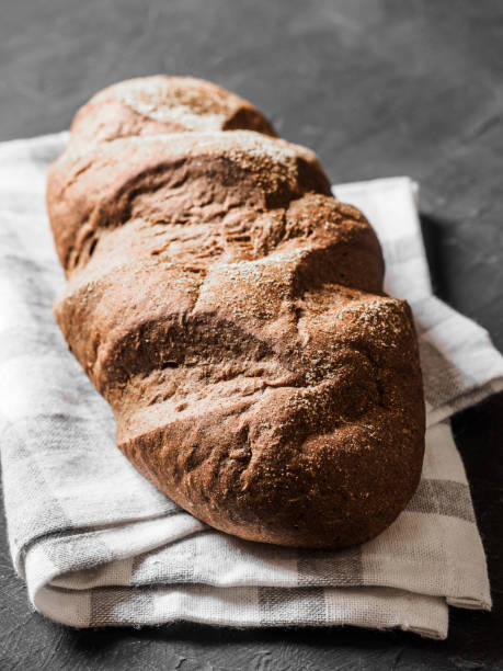 istock Loaf dark buckwheat bread on white textile napkin black table background. Fresh delicious homemade healthy bake. Bakery. 1220369349