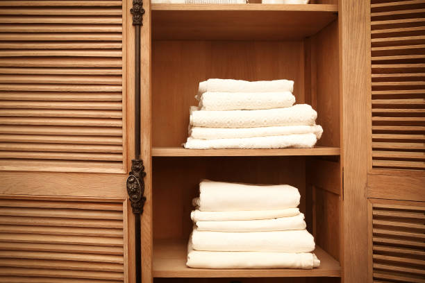 Stack of fresh white bath towels on bed sheet in modern hotel bedroom interior with window on background, copy space