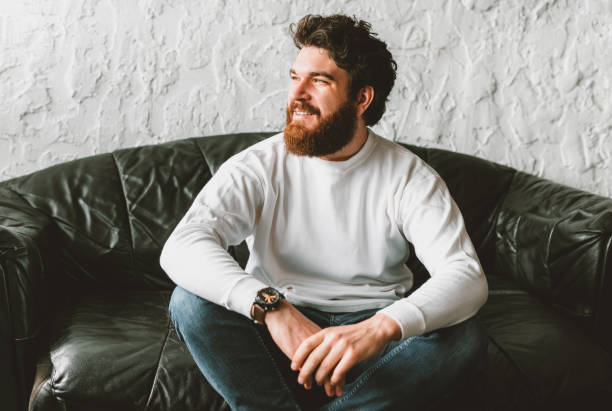 istock handsome bearded man looking away and sitting on sofa 1220371617
