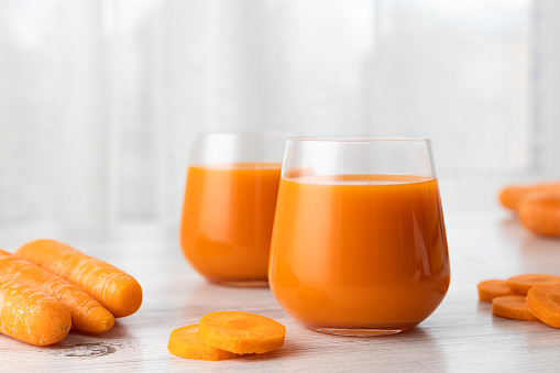 Two glasses with carrot juice on the table. Light background.