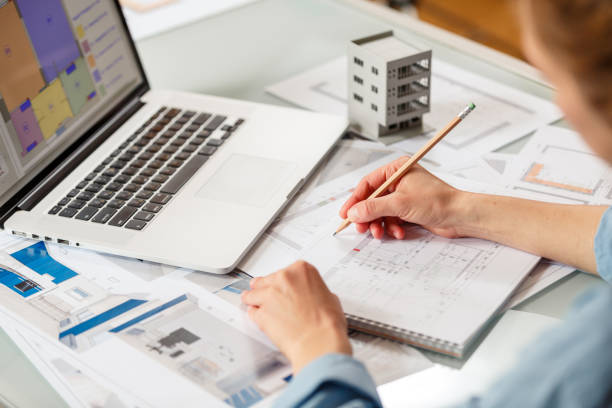 istock Interior designer working with an apartment plans in a studio, with blueprints and laptop on a table. 1220385258
