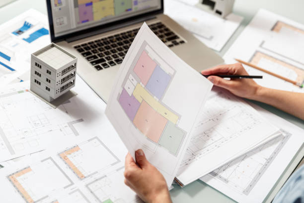 istock Interior designer working with an apartment plans in a studio, with blueprints and laptop on a table. 1220385268