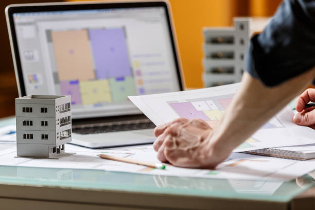 istock Interior designer working with an apartment plans in a studio, with blueprints and laptop on a table. 1220385299
