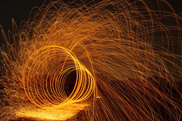 Photo of Image playing fireworks by rotating the wave shape of the lines, sparks to light. Amazing Fire Dance in the middle basin slope and beautiful reflection with copy space