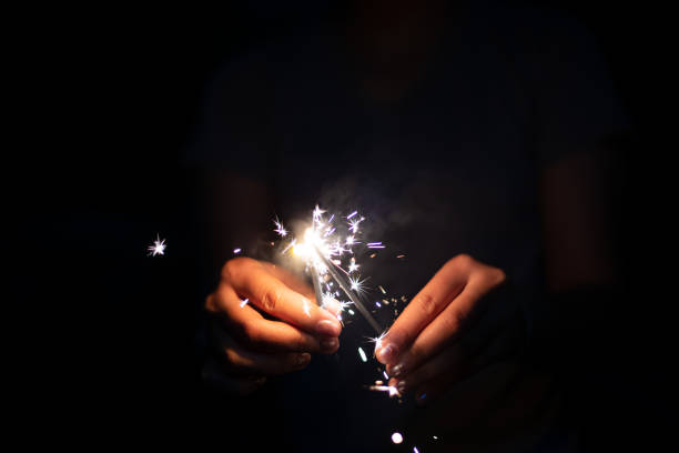 sparkler in front of purple colored blurred background for New Year's Eve / celebration navidad y año nuevo imagen concepto de vísperas con primer plano de un par de manos de hombre tomando una chispa de fuego rojo para celebrar la fiesta de la noche - centrarse en los fuegos artificiales y la esperanza para el futuro de la gente