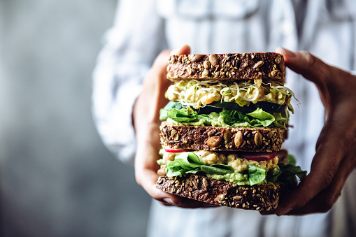 Close-up of a woman's hands holding a large vegetarian sandwich. Chef holding super vegan sandwich.