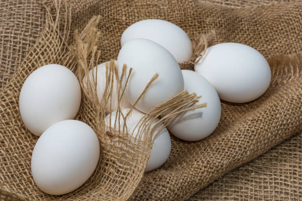 istock White chicken eggs wrapped in burlap next to a basket White eggs on burlap background 1220394716