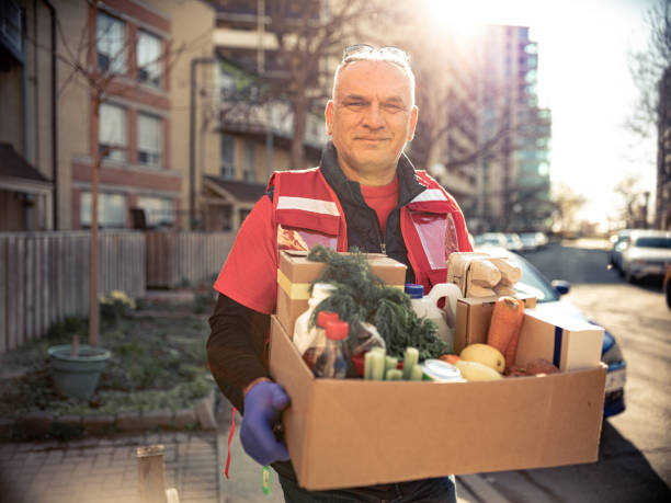 COVID-19, Donation Home food delivery during lockdown COVID-19, Mature Caucasian man -social worker volunteer  delivers  food during pandemic lockdown. Boxes of donated perishable food or fresh produce. Urban setting of a North American city. home delivery photos stock pictures, royalty-free photos & images
