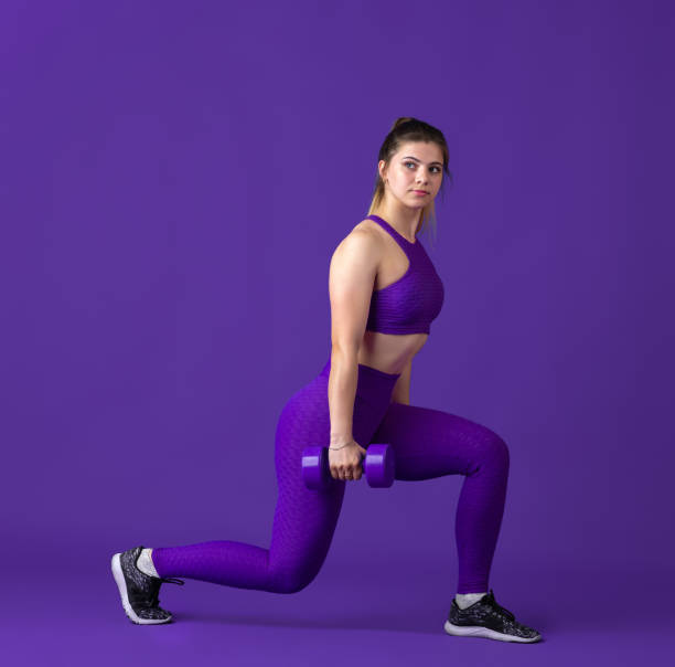 istock Beautiful young female athlete practicing on purple studio background, monochrome portrait 1220400117