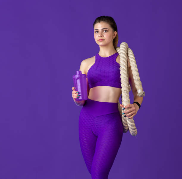 istock Beautiful young female athlete practicing on purple studio background, monochrome portrait 1220400147