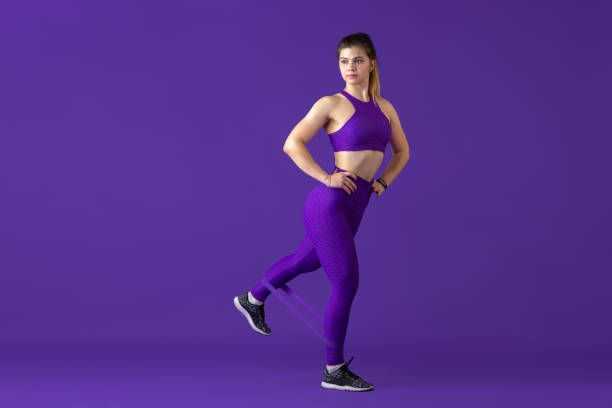 istock Beautiful young female athlete practicing on purple studio background, monochrome portrait 1220400154
