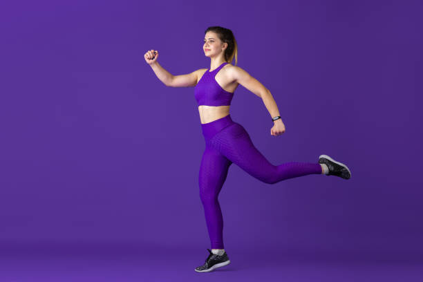 istock Beautiful young female athlete practicing on purple studio background, monochrome portrait 1220400197
