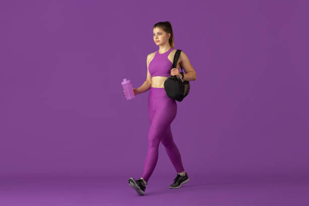 Beautiful young female athlete practicing on purple studio background, monochrome portrait