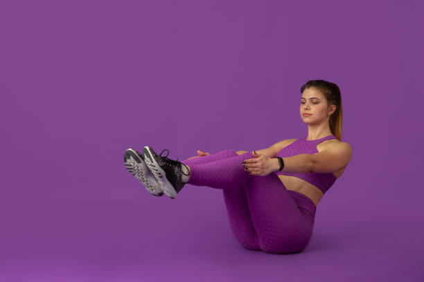 Beautiful young female athlete practicing on purple studio background, monochrome portrait