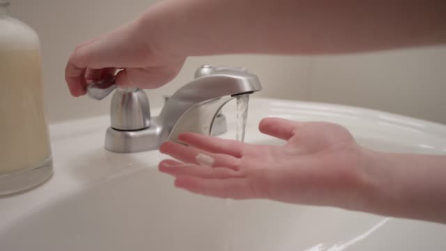 Close up of a sink and hands rinsing off soap under water in slow motion