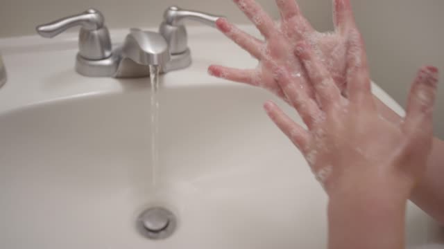 Close up of a sink and hands rinsing off soap under water in slow motion