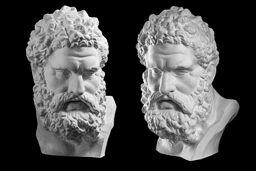 Two white bust of the Hercules. Heracles head sculpture, plaster copy of a marble statue isolated on a black background. Son of Zeus, the ancient Greek god. Ancient statue of hero.