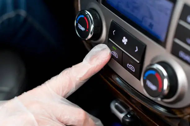 Photo of a hand in a medical glove presses the air recirculation button in the car