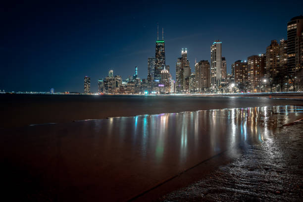 ville de chicago photographie de nuit d’horizon avec des lumières réfléchissant outre de l’eau stagnante échouée au-dessus de la rive en béton ondulée le long du lac michigan dans le centre-ville. - north avenue beach photos et images de collection