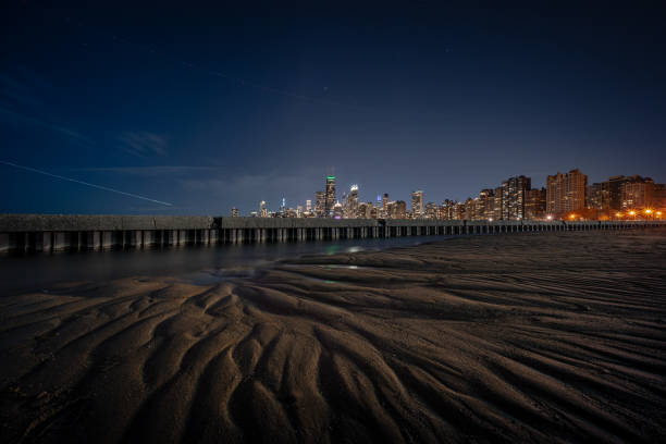 incroyable intéressant et belle ligne d’horizon de paysage urbain de chicago la nuit avec de magnifiques motifs de méandres au premier plan de crêtes et de ravins sculptés dans le sable de la plage en raison de l’érosion de l’eau en retrait. - north avenue beach photos et images de collection