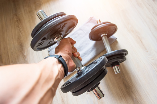 Male hand with a fitness bracelet clock holds a dumbbell, another dumbbell on the floor with a towel, home workout