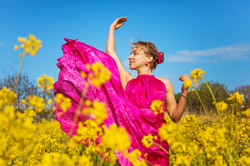 A beautiful woman wearing a pink dress in a outdoor field of yellow flowers under a blue summery sky