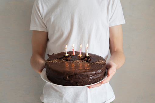 Male hands holding a plate with a festive chocolate cake and candles burning in it, happy birthday greetings concept, horizontal orientation