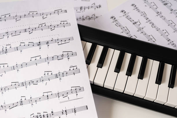 istock Selective focus of home synthesizer with sheet music (musical) notes on a white table. Piano keyboard. 1220412480