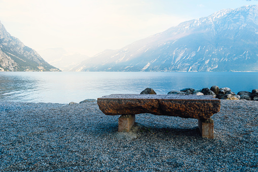 The stone bench on shore of valley of beautiful lake Garda among the mountains, lake Garda is located in the North of Italy.
