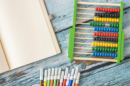 Wooden abacus, empty notebook and felt tip pens isolated on old blue wooden background