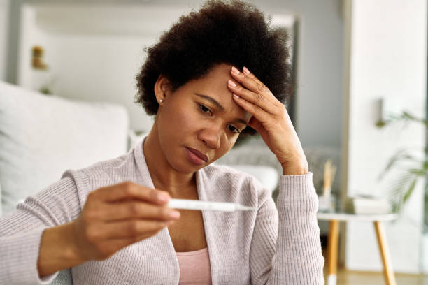 istock Distraught African American woman using thermometer and checking her temperature at home. 1220418131