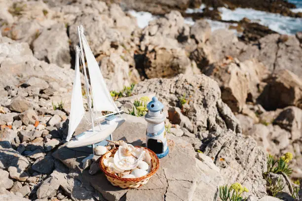 Toy wooden sailing boat and blue lighthouse and seafish plate on the rocky sea beach of the Adriatic Sea
