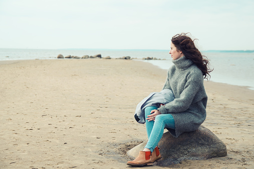 Attractive woman wearing a warm cardigan at the cold beach. Stock image.