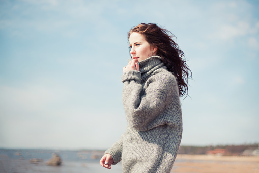 Attractive woman wearing a warm cardigan at the cold beach. Stock image.