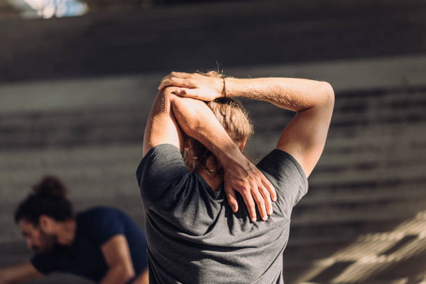 Back View of a Blond Man Warming up for a City Run With Friends Man stretches his arm while warming up for an outdoor cardio workout. warming up stock pictures, royalty-free photos & images