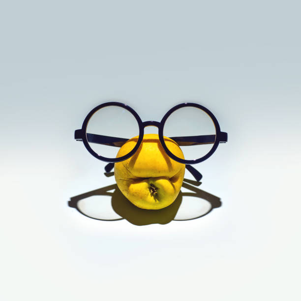 istock Yellow shrivelled apple with a grimace in glasses. On a light blue background 1220426267