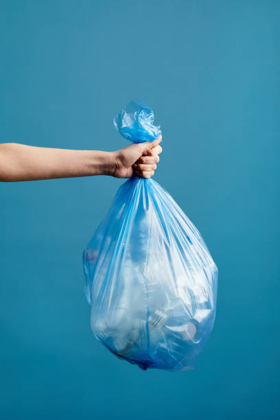 Hand Holding Garbage Bag Vertical image of female hand holding trash bag with plastic against blue background, waste sorting and recycling concept, copy space garbage bag stock pictures, royalty-free photos & images