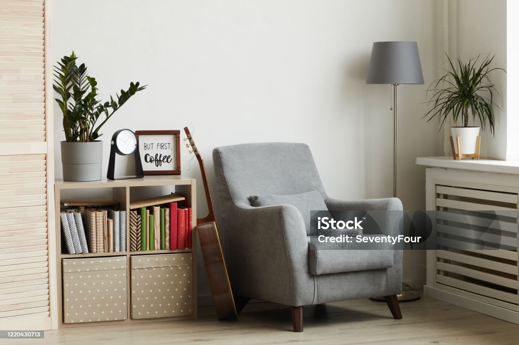 Inviting Reading Nook Background image of cozy reading nook in modern minimal interior, focus on grey armchair against white wall, copy space Corner Stock Photo