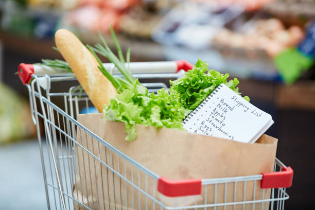 Shopping Cart in Grocery Store Background image of shopping cart with fresh groceries, focus on shopping list in paper bag, copy space fruit cart vendor stock pictures, royalty-free photos & images