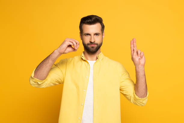 istock Handsome man showing letters in sign language language on yellow background 1220435824