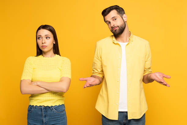 istock Confused man standing near spherical girlfriend on yellow background 1220435877