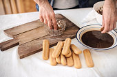 Quarantine cooking: a man is soaking ladyfinger-biscuits in coffee to prepare tiramisu