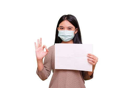 Isolated Portrait of a cheerful and healthy young woman asian wearing medical mask holding a empty sheet of paper.