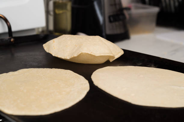 Handmade corn (maize) tortillas puffing up while cooking on a griddle at a mexican market.