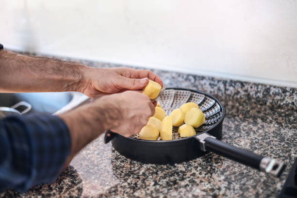 quarantine cooking: a man is peeling potatoes and put them in the pot - camel back imagens e fotografias de stock