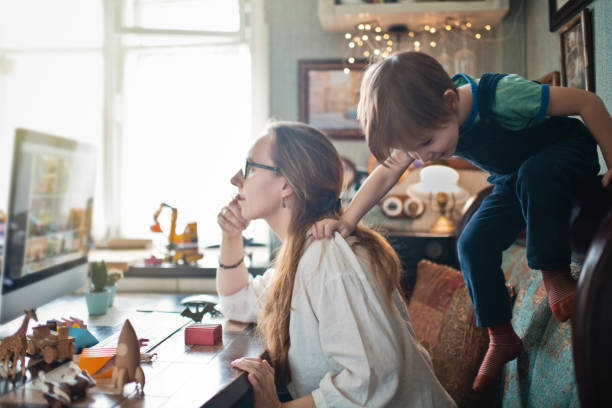 Woman working from home during quarantine with her little son all around Mother with her boy home with self-isolation, trying to work remotely children misbehaving stock pictures, royalty-free photos & images