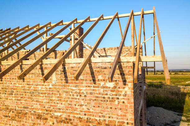 Unfinished brick house with wooden roof structure under construction.