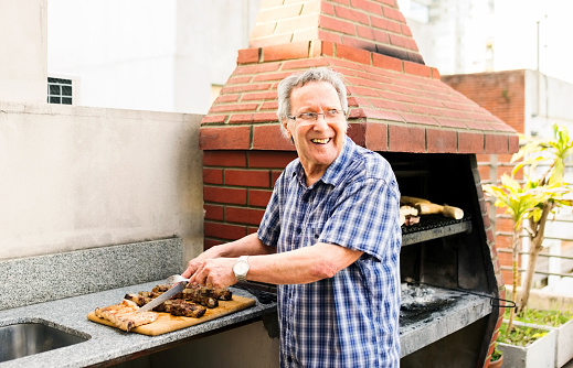 Shot of a senior man preparing meat on barbecue for lunch in the backyard